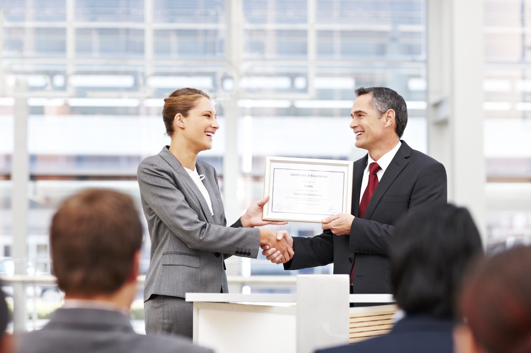 Businesswoman shakes the hand of a man giving her an award on stage. Horizontal shot.