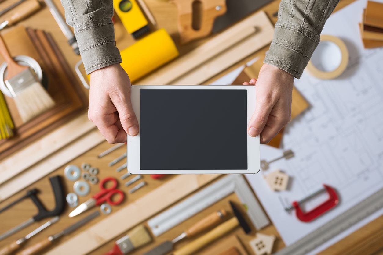 Male hands holding a digital tablet, work table with tools and project on background, home renovation and do it yourself concept