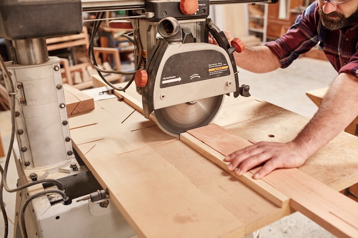 Cropped shot of a carpenter using a radial arm circular saw to cut a plank of wood, in his woodwork studio